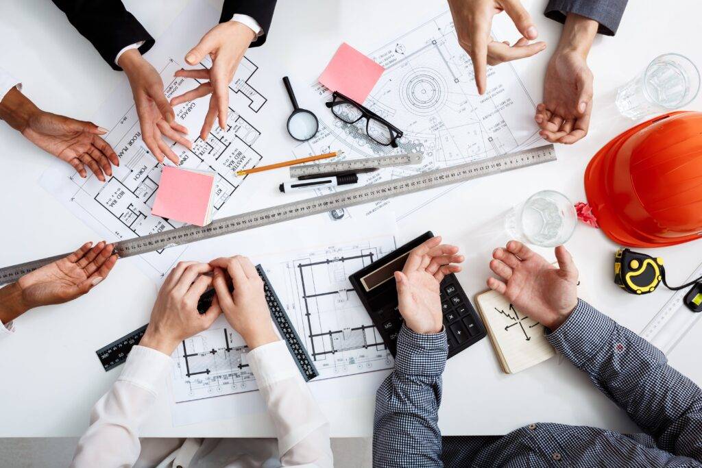 5 people are consulting over a house plan sheet on the tabletop.